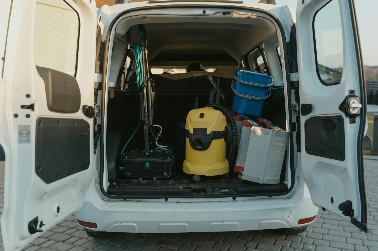 A van with cleaning supplies reveals its open trunk filled with tools and equipment.